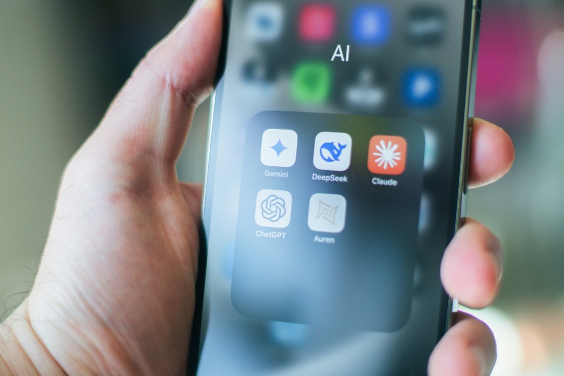 Hand hält ein Smartphone mit einem App-Ordner voller KI-Assistenten