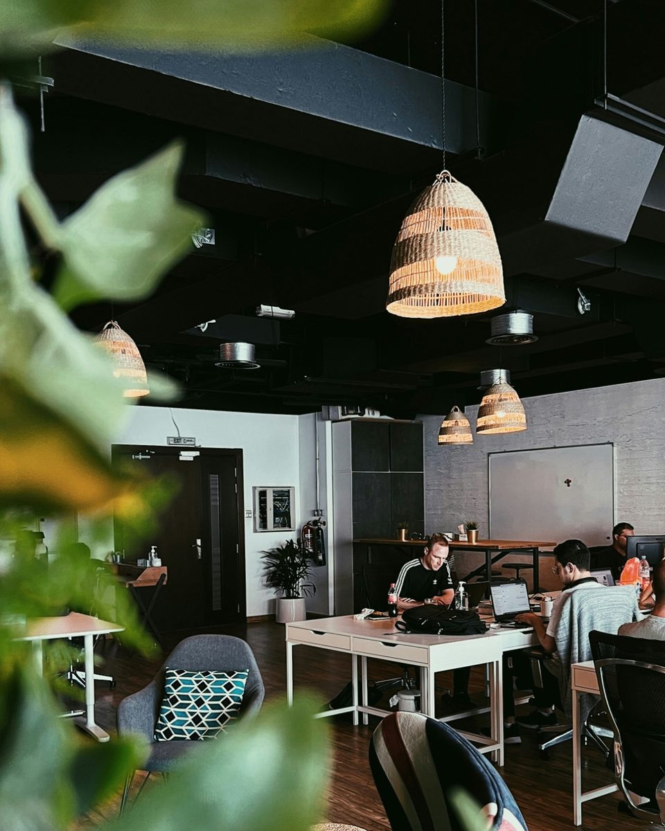 Offenes Büro mit mehreren Arbeitsplätzen, im Hintergrund arbeiten Menschen an Laptops