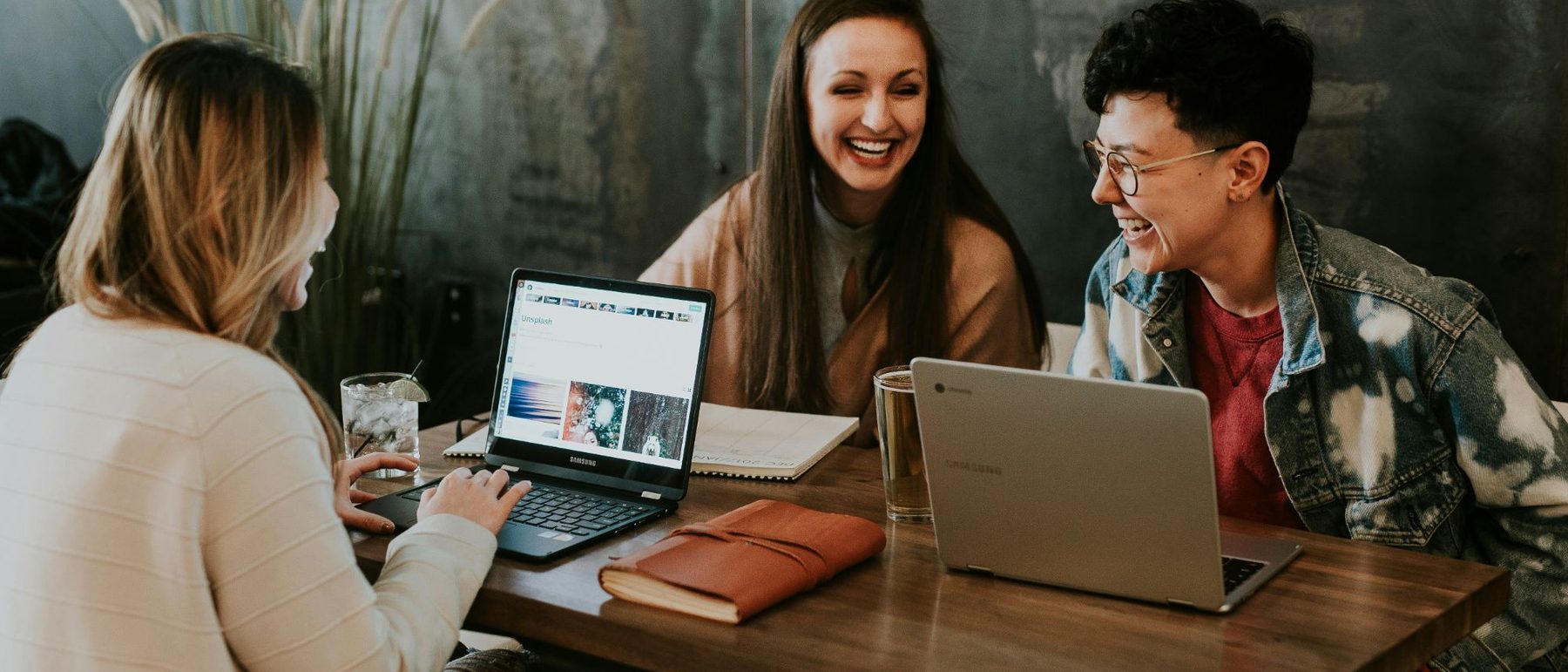 Drei Menschen sitzen lachend mit Laptops an einem Tisch